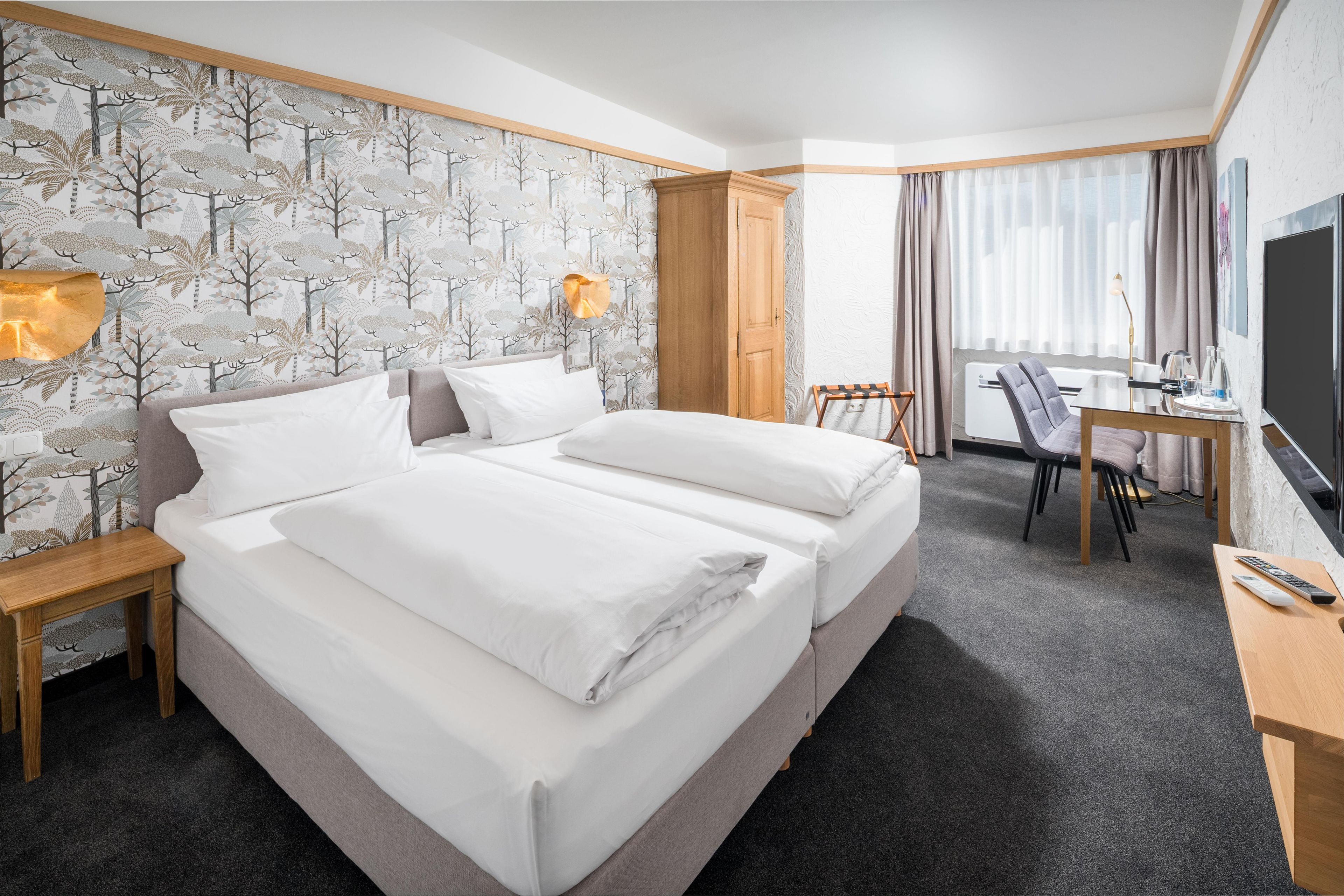 Habitación de hotel con una cama grande, un escritorio, una silla, un televisor y una ventana con cortinas.
