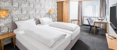 Habitación de hotel con una cama grande, un escritorio, una silla, un televisor y una ventana con cortinas.