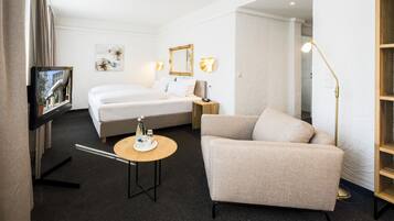 A hotel room with a bed, a sofa, a small table, a TV, and a lamp.