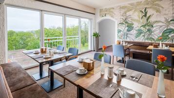 A dining area with tables, chairs, and a view of greenery outside.