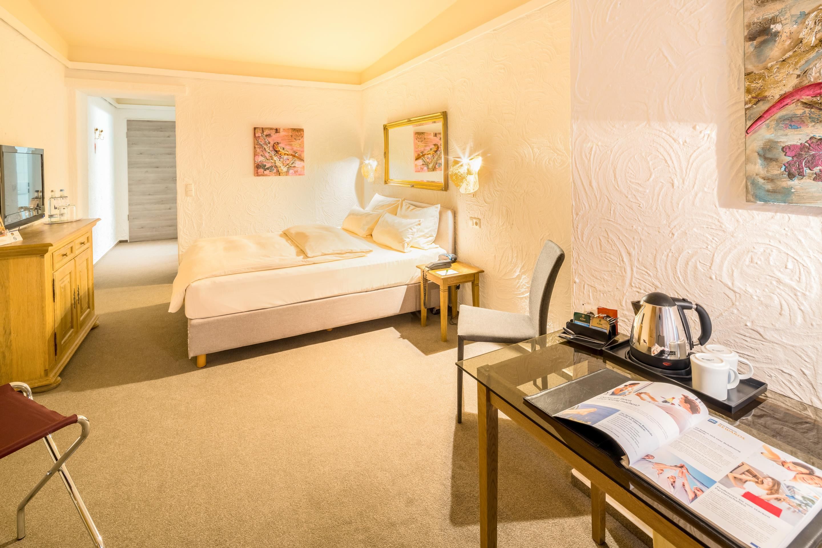 Habitación de hotel con cama, escritorio con cafetera, silla, televisor y puerta que da a otra habitación.