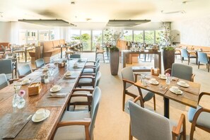 A spacious dining area with multiple tables and chairs, large windows, and potted plants. - Best Western Hotel Mainz (Mainz)