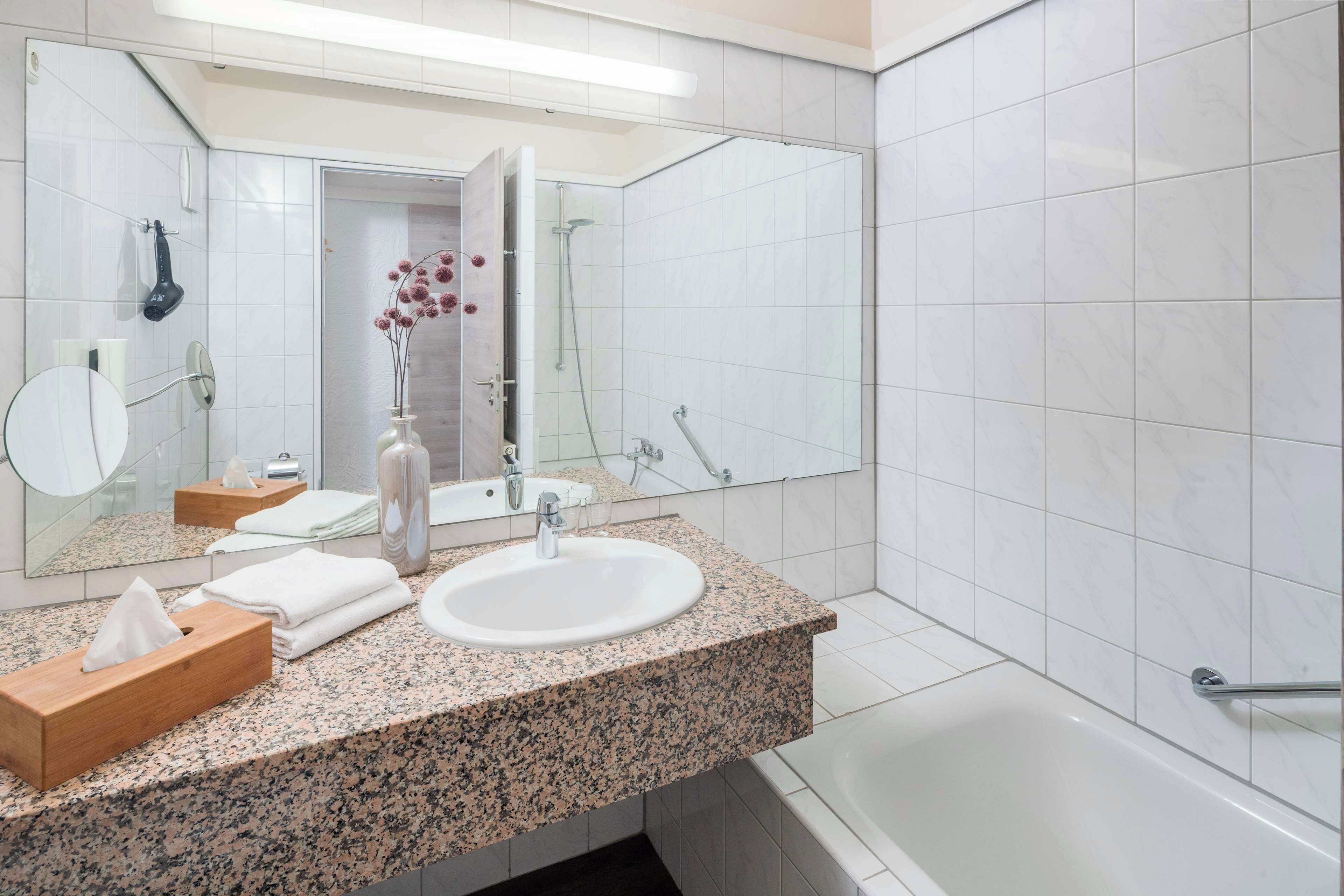 A modern bathroom with a granite countertop, white sink, and a large mirror.