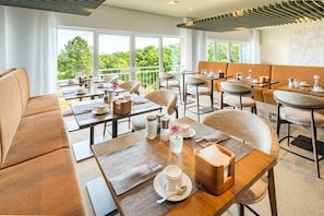 A modern dining area with multiple tables and chairs, large windows offering a view of greenery, and a contemporary ceiling design. - Best Western Hotel Mainz (Mainz)