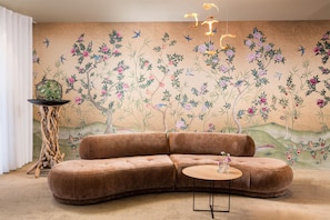 A room with a curved brown sofa, a round wooden coffee table, a decorative floor lamp, and a wall mural with birds and flowers. - Best Western Hotel Mainz (Mainz)