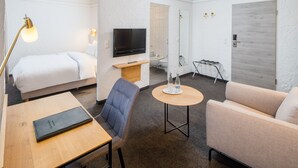 Quarto de hotel com cama, televisão, sofá, mesa pequena e cadeira.