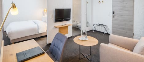 Una habitación de hotel con cama, televisión, sofá, mesita y silla.