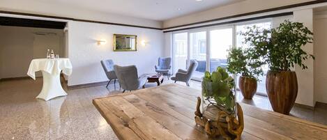 Una habitación amplia con una mesa de madera, dos sillones grises, una mesa cubierta con mantel blanco y un gran ventanal con luz natural.