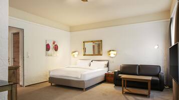 Ein Hotelzimmer mit einem Bett, einer Couch, einem kleinen Tisch, einem Spiegel und Wandleuchten.