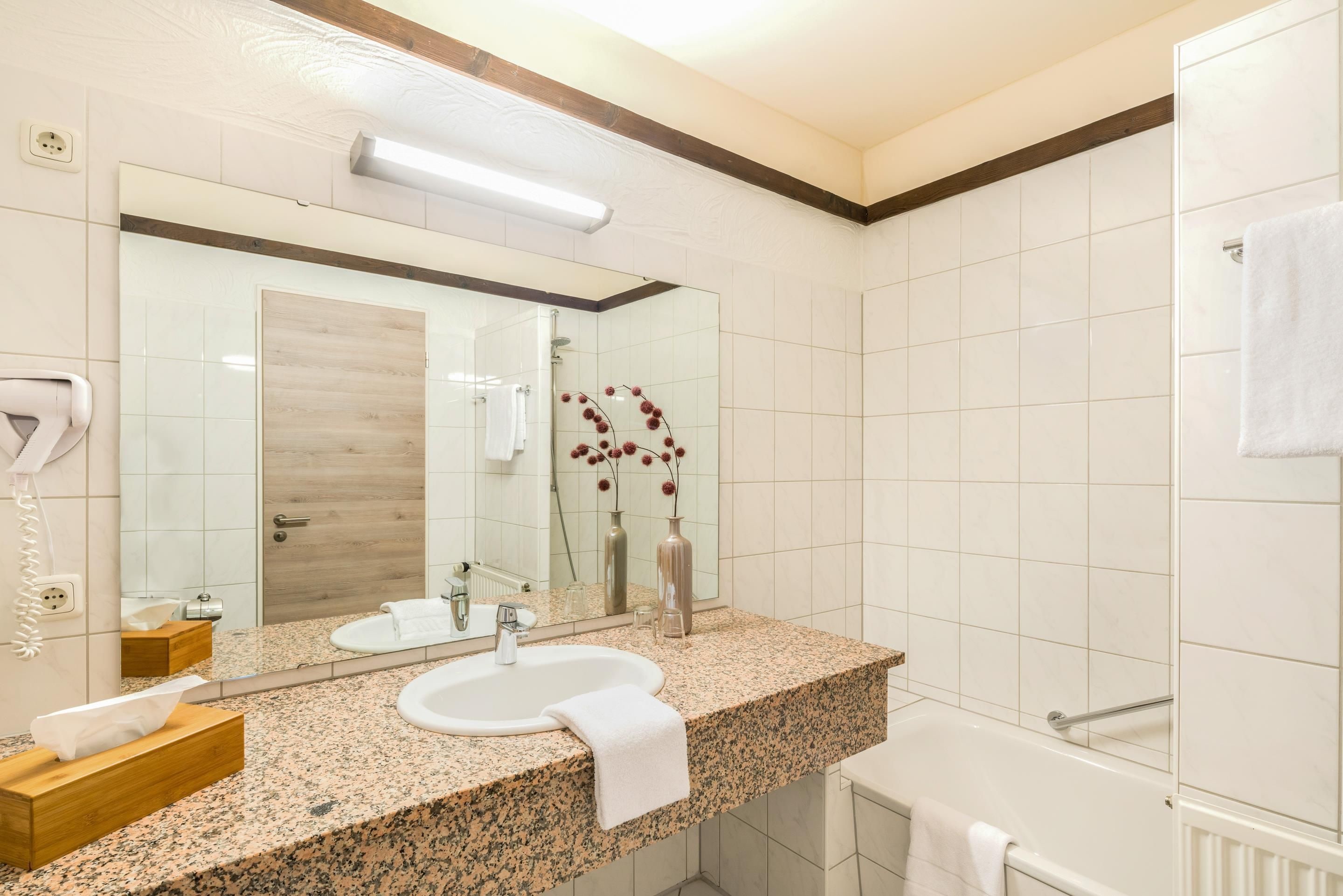 A modern bathroom with a granite countertop, a large mirror, a shower, and a towel rack.