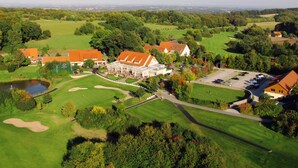 A golf course with a clubhouse, a pond, and surrounding greenery. - Court Hotel (Halle Westphalia)