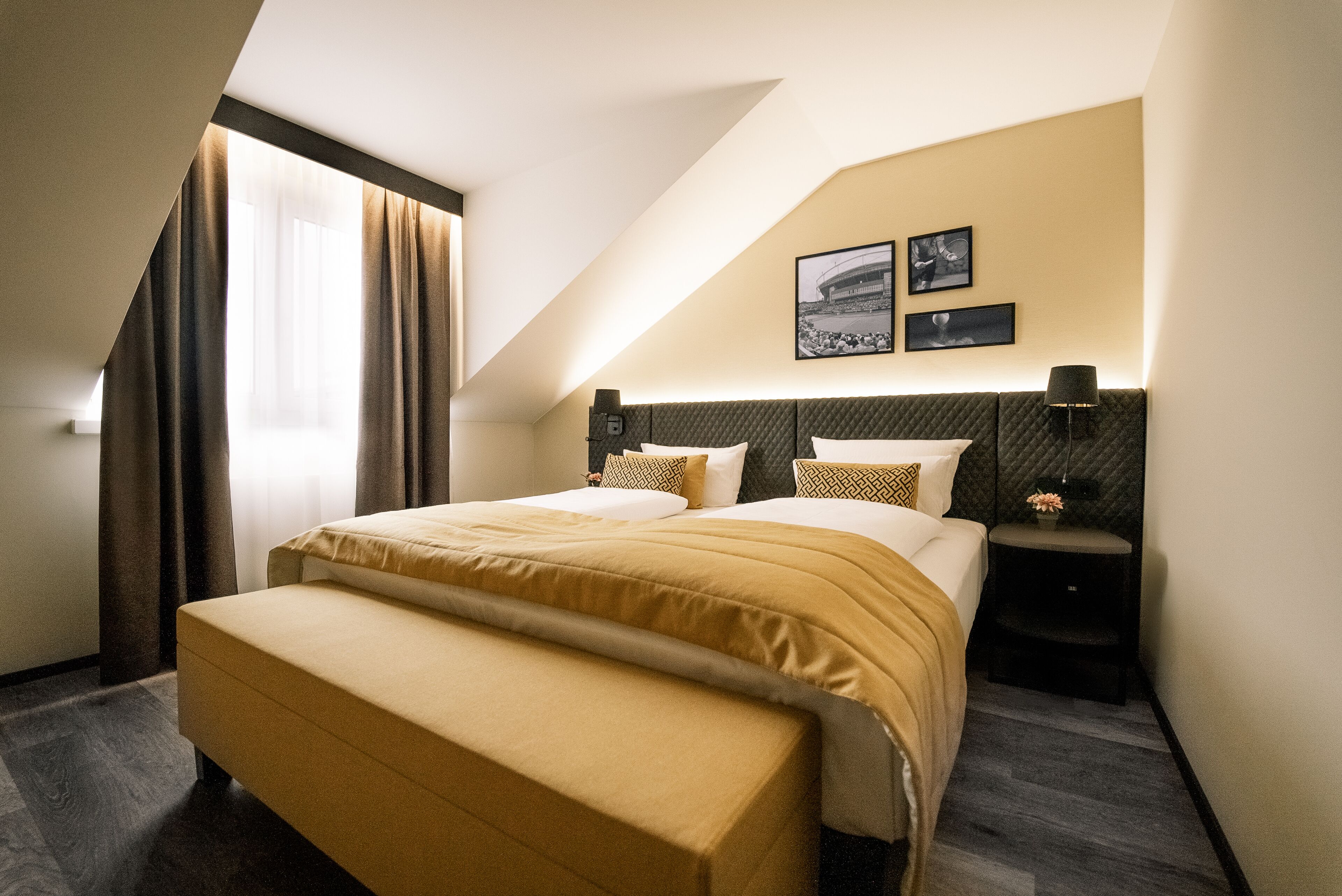 A hotel room with a bed, a bench, a nightstand, and a wall-mounted lamp.