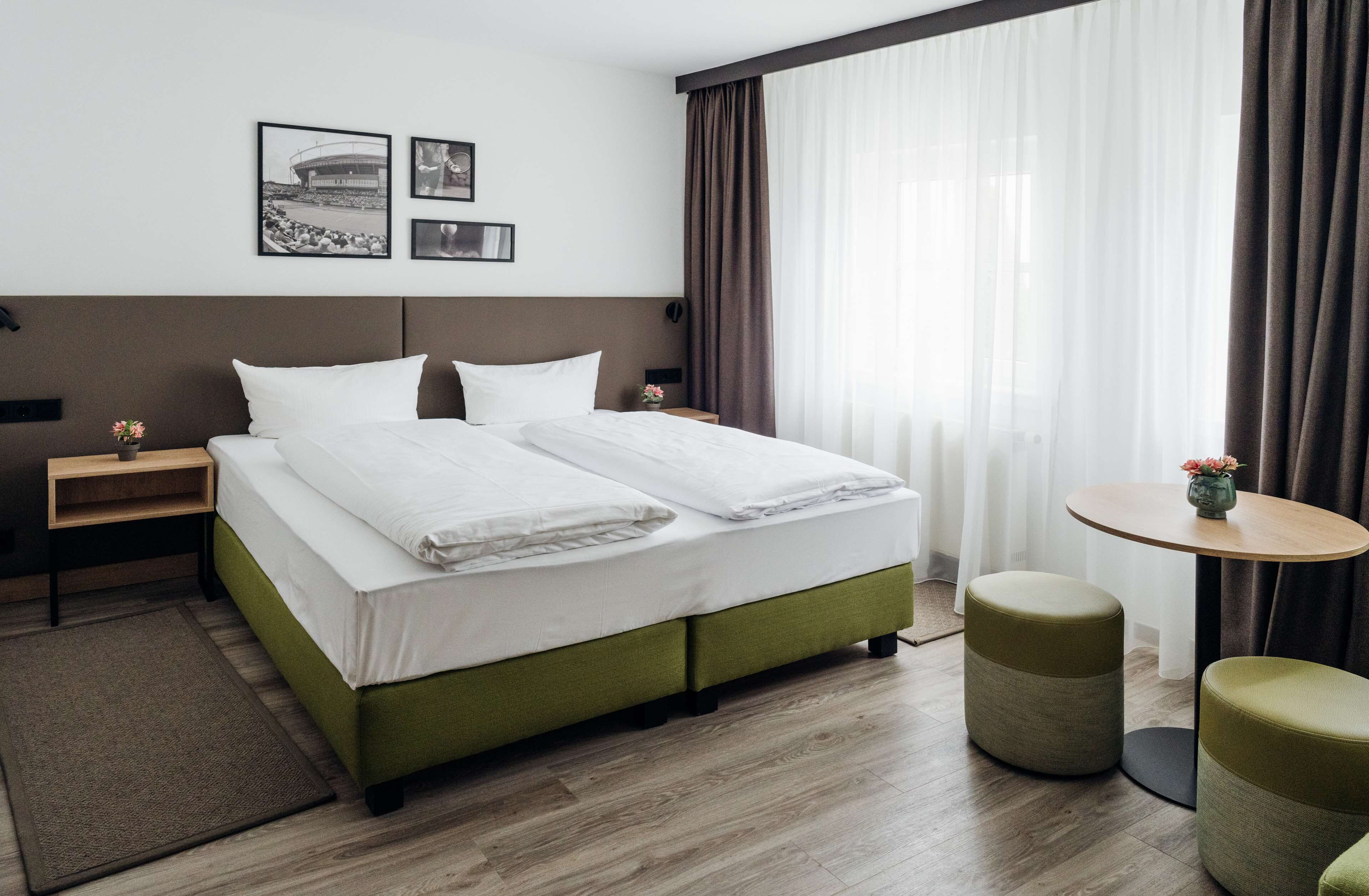 A hotel room with a large bed, two bedside tables, a small round table, and two ottomans.