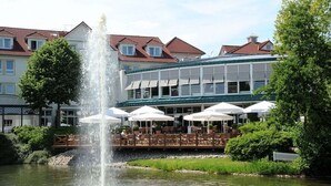 A fountain in a courtyard with outdoor seating and a building in the background. - Court Hotel (Halle Westphalia)