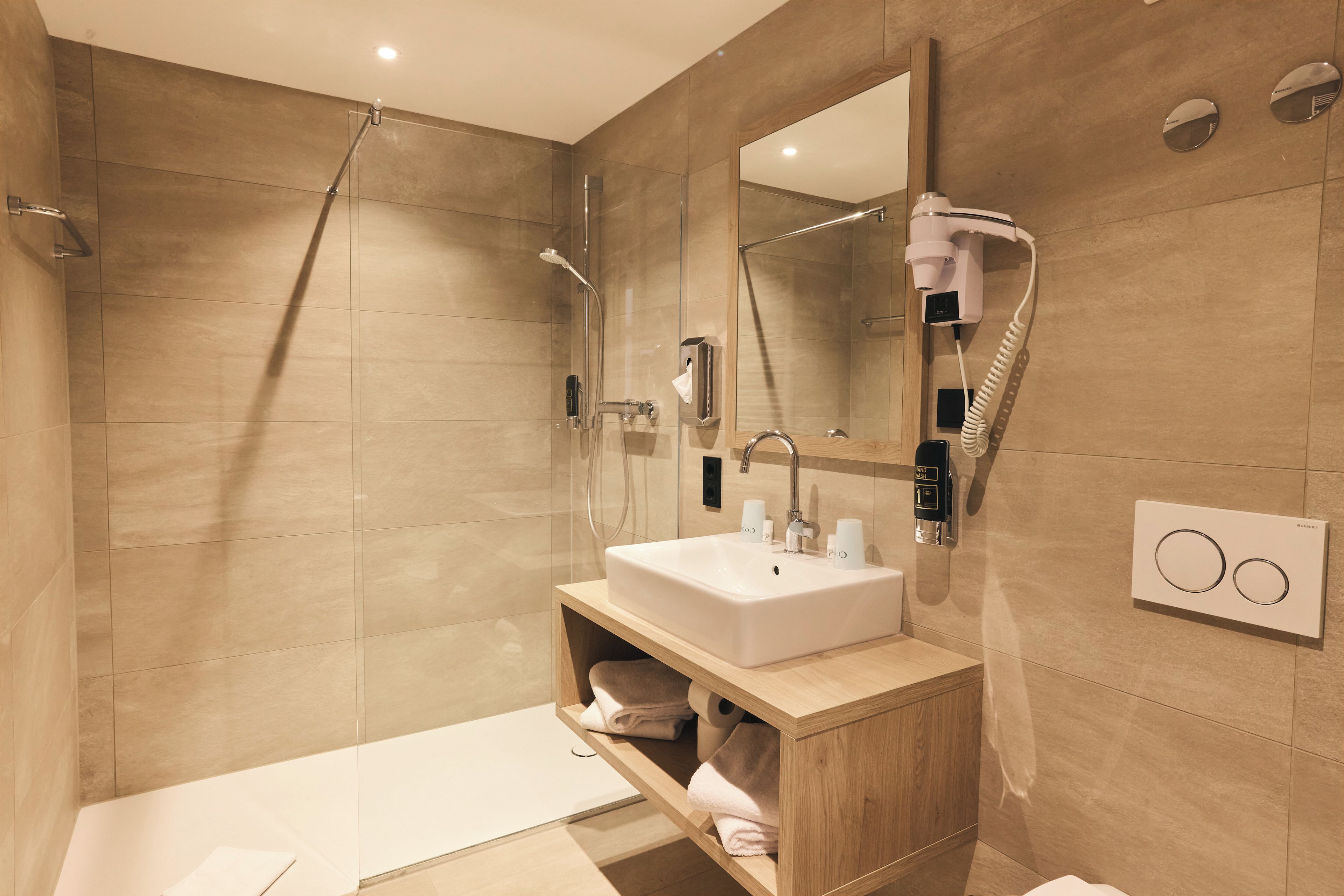 Ein modernes Badezimmer mit einer gläsernen Duschkabine, einem integrierten Waschbecken und einem Waschtisch mit Handtuchhalter.