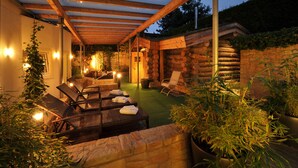 An outdoor patio with wicker furniture, a stone wall, and a wooden pergola. - Court Hotel (Halle Westphalia)