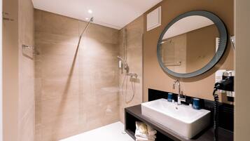 Een moderne badkamer met een douche met glazen wand, een grote ronde spiegel en een witte wastafel met een zwart aanrecht.