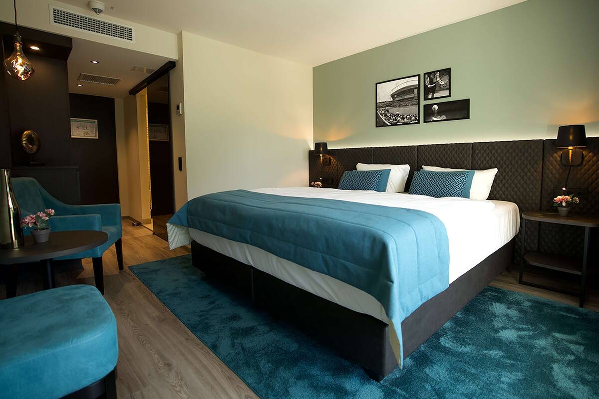 A modern hotel room with a large bed, a seating area with a chair and table, and artwork on the walls.