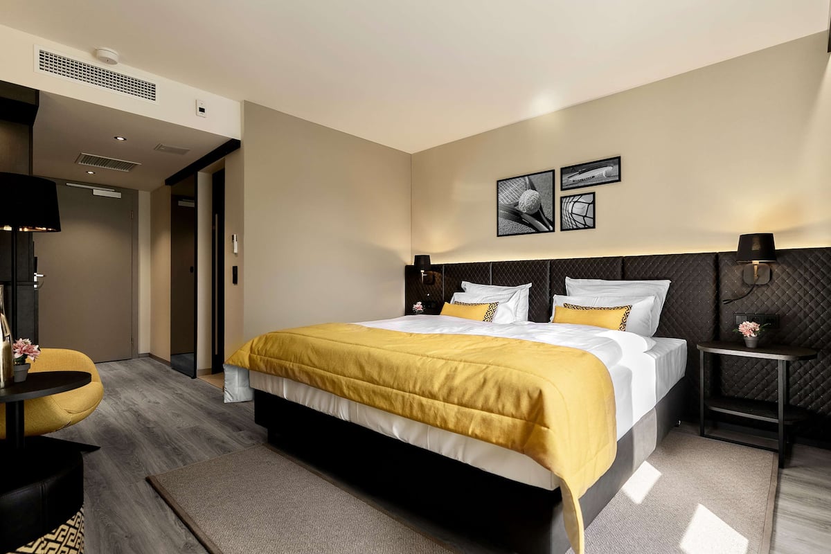 A modern hotel room with a large bed, a bedside table, a chair, and a television.