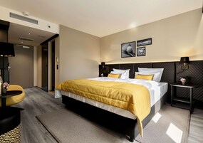 Una habitación de hotel moderna con una cama grande, una mesita de noche, una silla y un televisor.