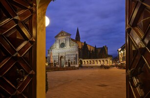 Un edificio storico con una cupola centrale e finestre ad arco, visibile attraverso un'apertura di una porta in legno.