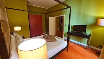 A room with a four-poster bed, a television on a stand, a red wardrobe, and a door leading to another room.