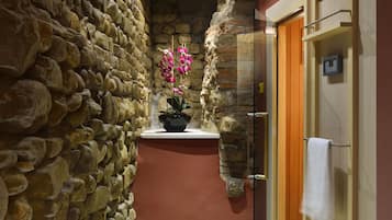 A stone wall corridor with a potted orchid and a towel hanging on a door.