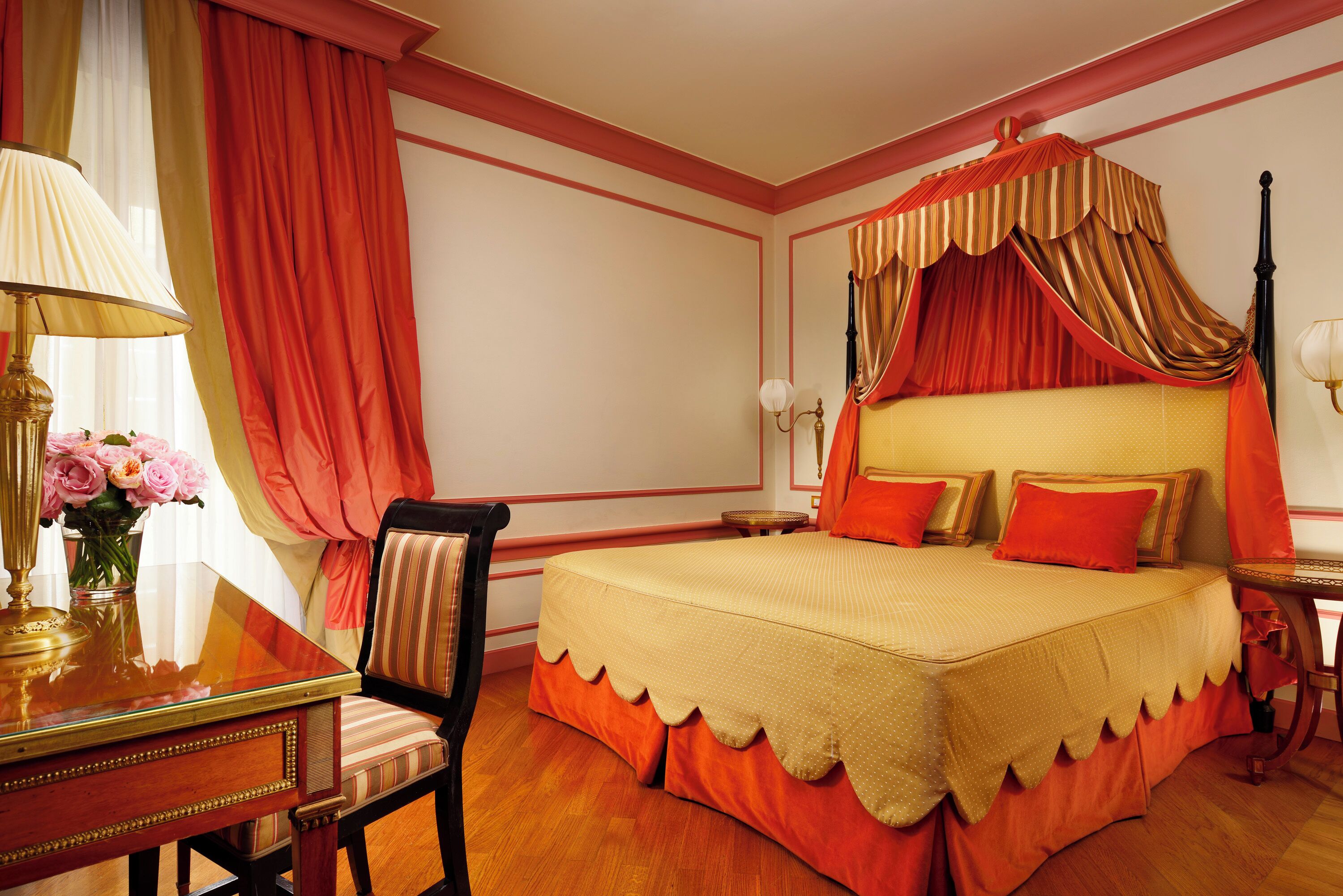 A bedroom with a canopy bed, a desk with a lamp, and a chair.
