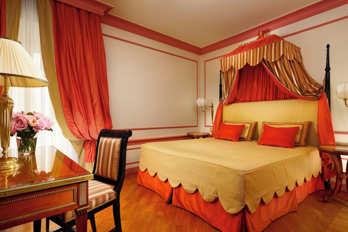 A bedroom with a canopy bed, a desk with a lamp, and a chair.