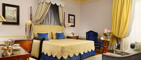 A bedroom with a four-poster bed, a desk with a chair, a small table with a vase of flowers, and a sofa.