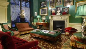 Una habitación con una pared verde, una chimenea, un sofá verde, un sillón rojo y una mesa de centro de madera con libros.