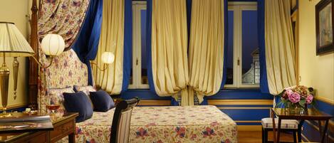 Una habitación con cama, escritorio, silla y ventana con cortinas.
