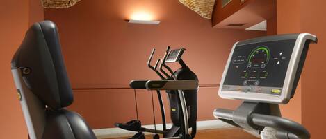 A gym with exercise equipment, including a stationary bike and a rowing machine, in a room with orange walls and a wooden floor.