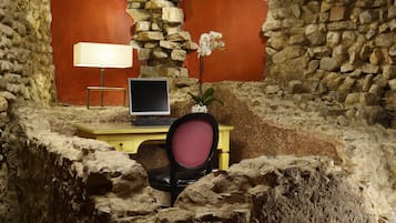 Una habitación con pared de piedra, un escritorio con computadora, una silla y una lámpara.
