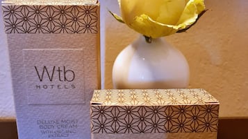Deux boîtes Wtb Hotels, l’une pour la crème pour le corps et l’autre pour le savon, avec un vase contenant une fleur jaune en arrière-plan.