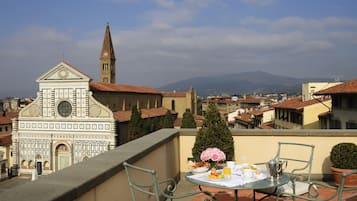 A terrace with a table set for breakfast, overlooking a historic building with a clock tower and a church.
