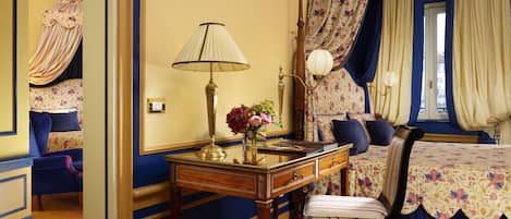 Une chambre à coucher avec un lit à baldaquin, un bureau avec une lampe, une chaise et une table de chevet agrémentée de fleurs.