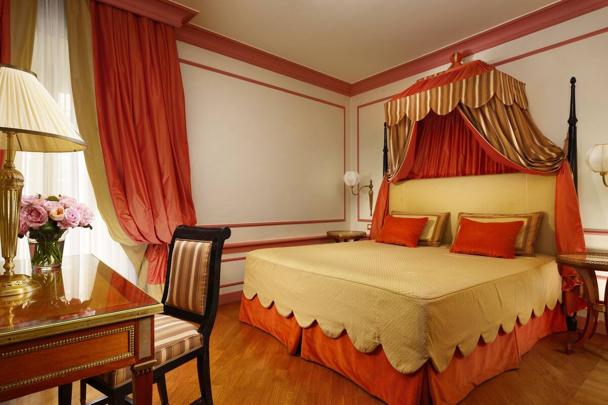 A bedroom with a canopy bed, a desk with a lamp, and a chair.