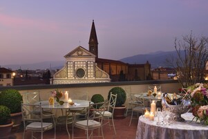 An outdoor terrace with tables and chairs, candles, and a decorative silver bowl with bottles.