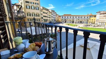 En balkon med et morgenbord, der kigger ud over et torv med historiske bygninger og en fontæne.