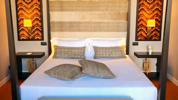 Una cama con dosel, con una colcha blanca y dos almohadones decorativos, flanqueada por dos mesitas de noche con lámparas.