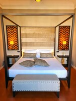 A four-poster bed with a white bedspread and two decorative pillows, flanked by two bedside tables with lamps.