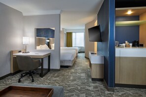 A hotel room with a desk, chair, two beds, a TV, and a kitchenette.