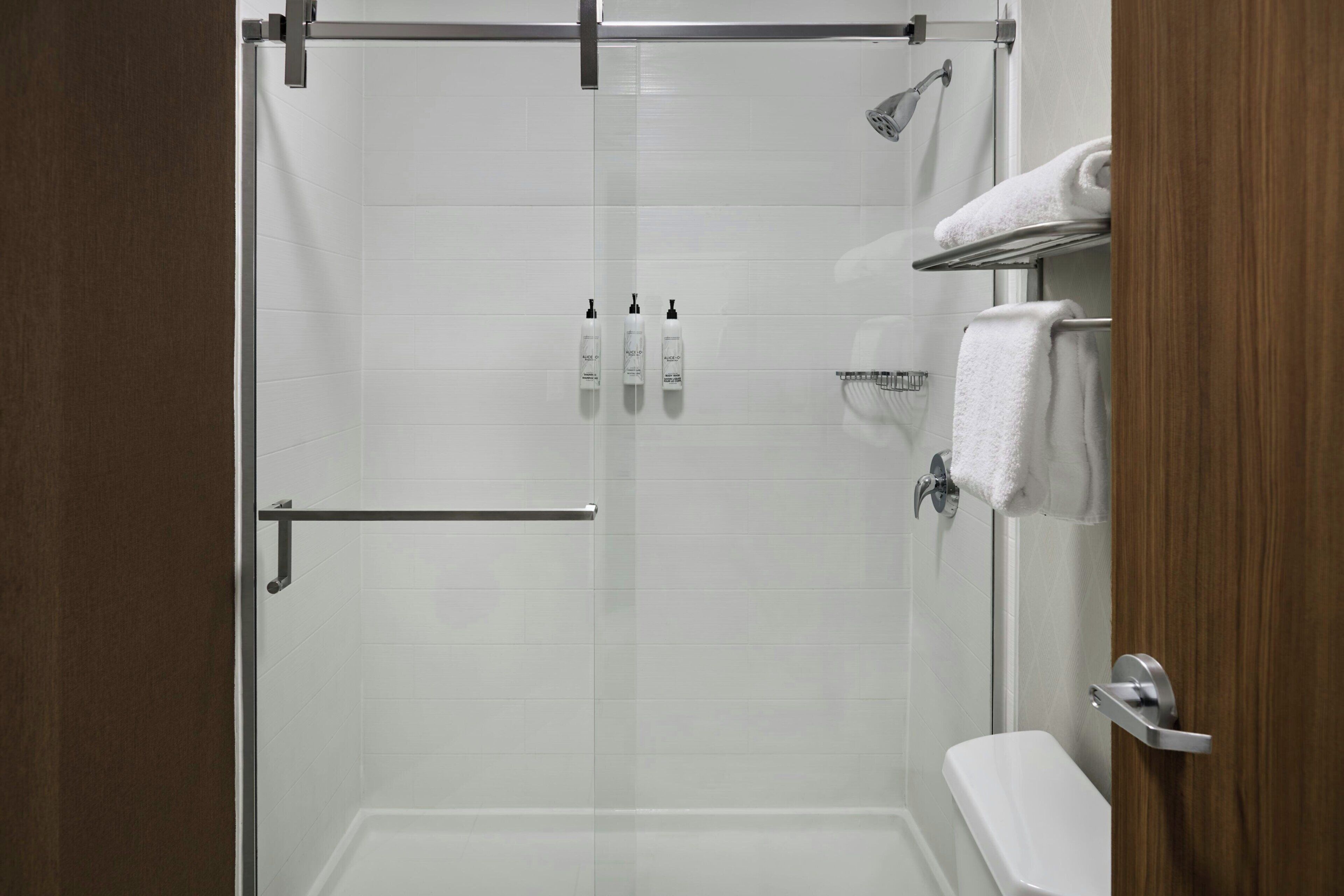 A modern shower area with a glass door, a handheld showerhead, and a towel rack.