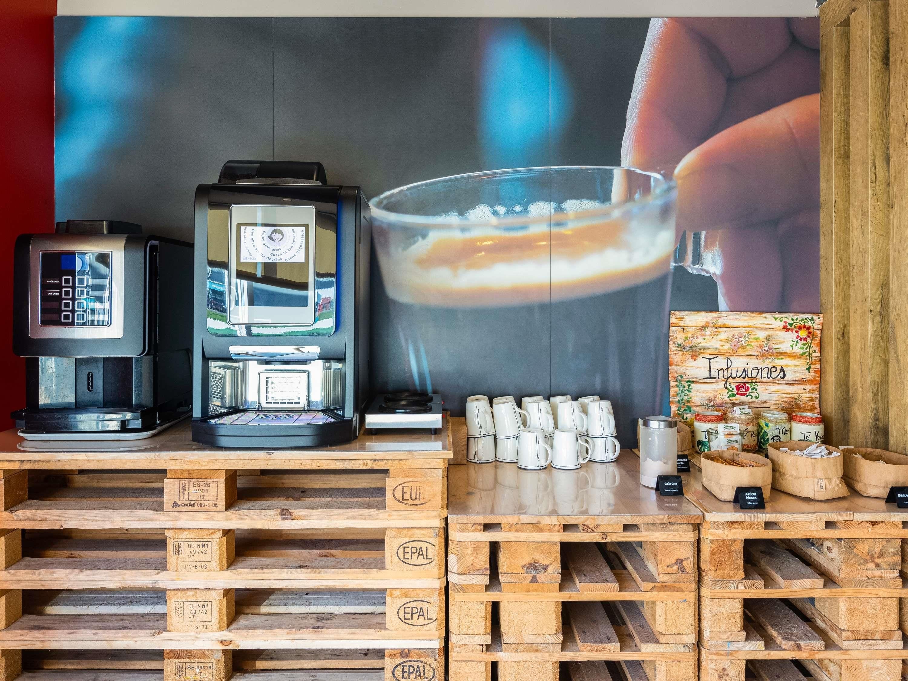 A coffee station with a digital coffee machine, a glass of coffee, and a display of coffee mugs and jars.
