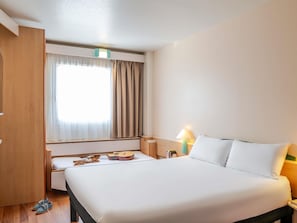 A hotel room with a bed, a bedside table with a lamp, a window with curtains, and a wooden wardrobe. - ibis Bilbao Barakaldo (Barakaldo)