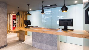 A reception desk with two monitors, a wooden counter, and pendant lighting. - ibis Bilbao Barakaldo (Barakaldo)