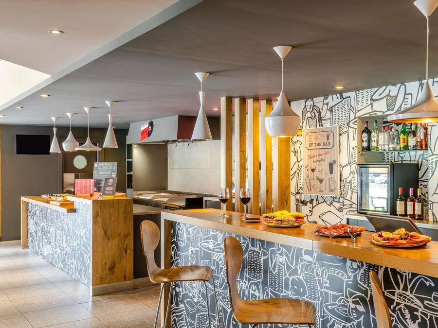 A modern bar area with a central island, bar stools, hanging pendant lights, and a wall with a food and drink illustration.