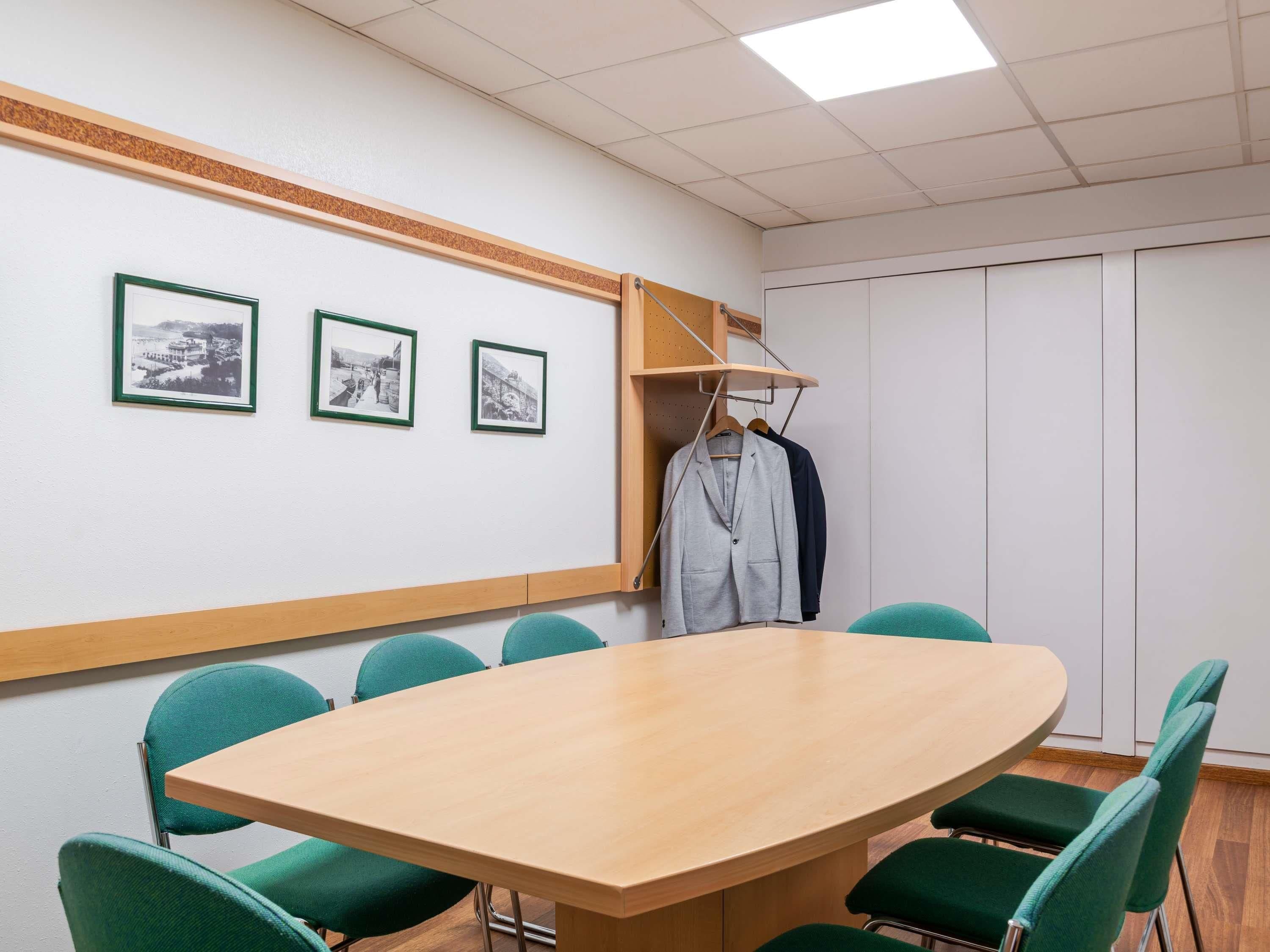 Un salón de conferencias con una mesa de madera, sillas verdes y tres cuadros en la pared.