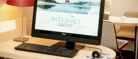 En datorskärm som visar en hotellsida med texten ”Gratis internet”, ett tangentbord, en mus och en röd lampa på ett skrivbord.